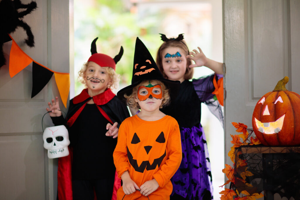 Kids trick or treat on Halloween night. Child at decorated house door. Boy and girl in witch and vampire costume and hat with candy bucket and pumpkin lantern. Autumn decoration. Friends play.